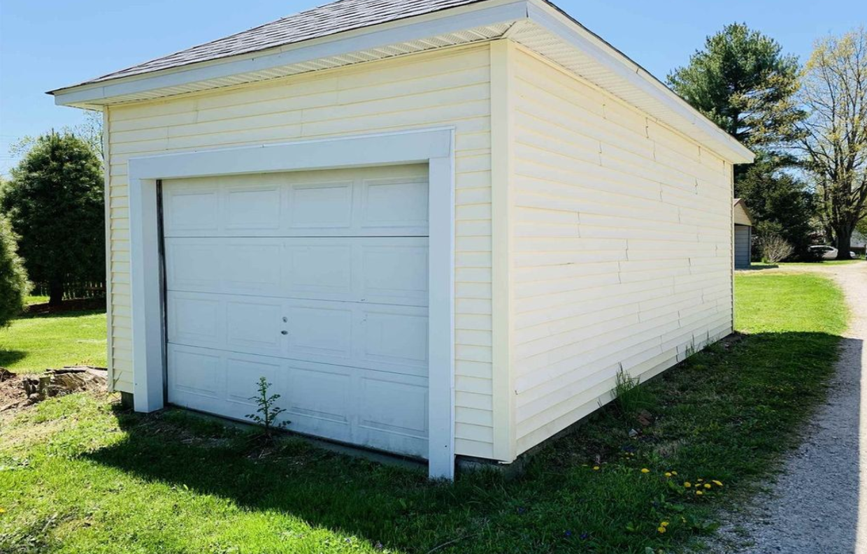 A white garage with a white door is sitting in the middle of a grassy field.