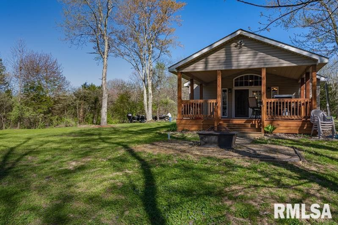 A small house with a porch in the middle of a grassy field.