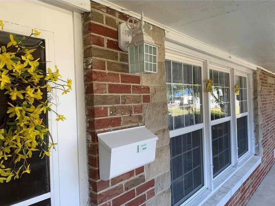 A white mailbox is on the side of a brick building.