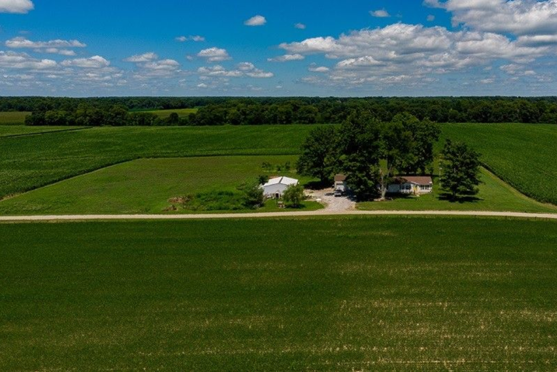 An aerial view of a farm with a house in the middle of a lush green field.