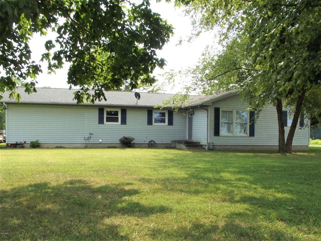 A white house with black shutters is sitting in the middle of a lush green field.