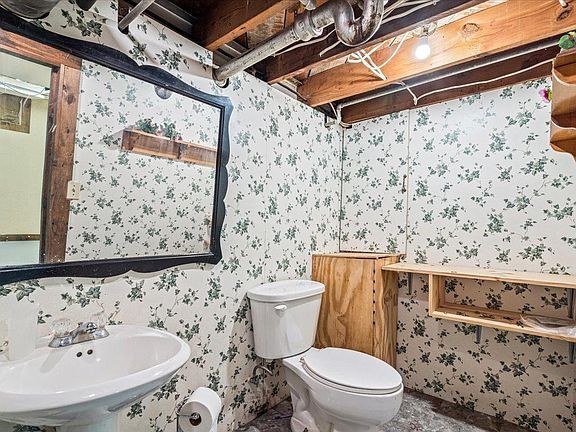 A bathroom with a toilet , sink , mirror and floral wallpaper.
