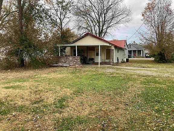 A small white house with a red roof is sitting in the middle of a grassy field.