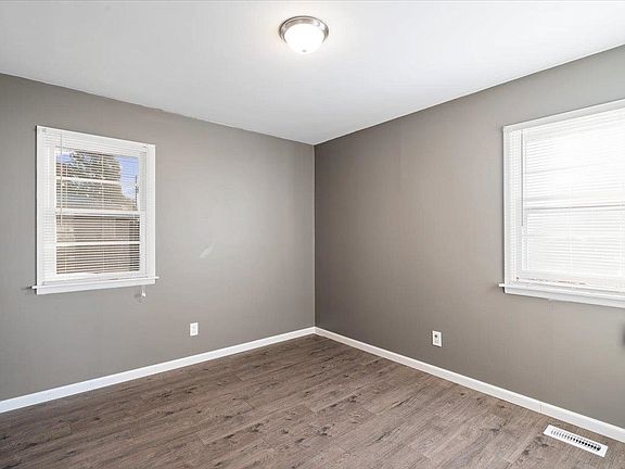An empty room with gray walls and wooden floors and two windows.