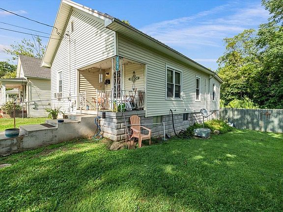 A small white house with a porch and a chair in the backyard.