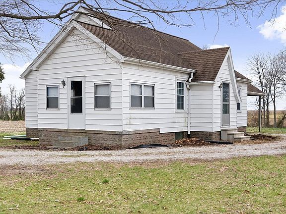 A small white house with a brown roof is sitting in the middle of a grassy field.