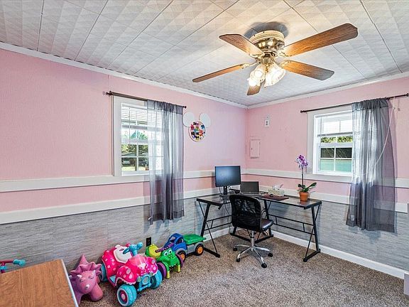 A room with pink walls , a desk and a ceiling fan.