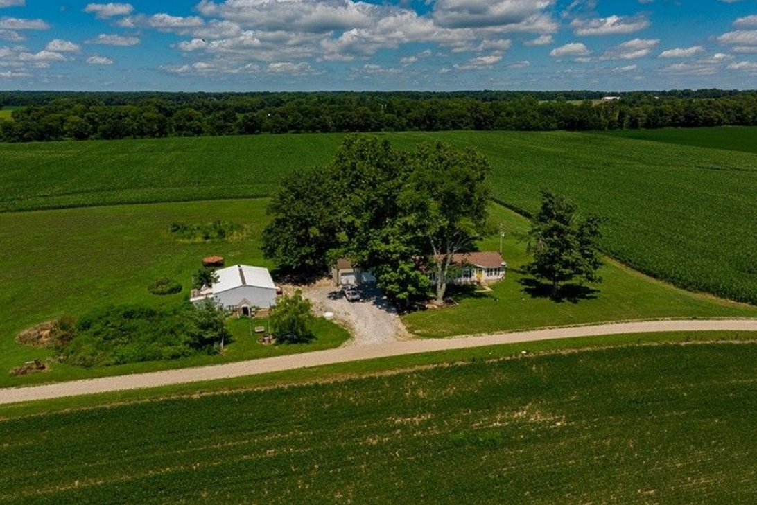 An aerial view of a house in the middle of a lush green field.