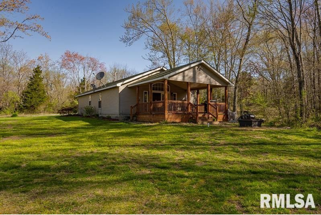 A small white house with a porch in the middle of a lush green field.