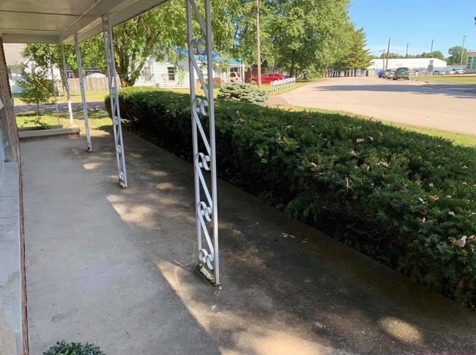 A porch with a white awning over it is surrounded by bushes and trees.