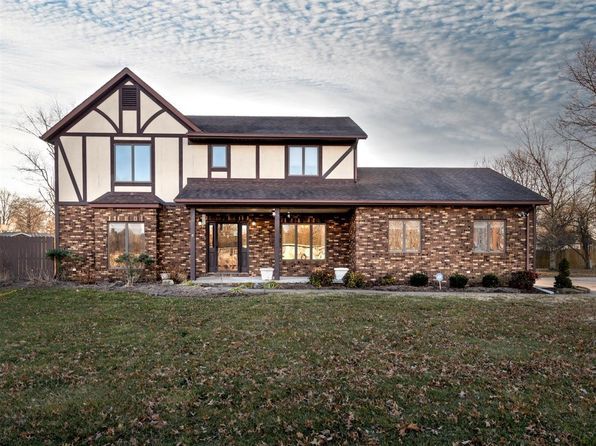 A large brick house with a black roof is sitting on top of a lush green field.