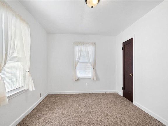 An empty bedroom with a carpeted floor , two windows and a door.