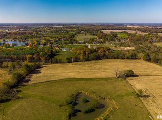 An aerial view of a lush green field with trees and a pond.