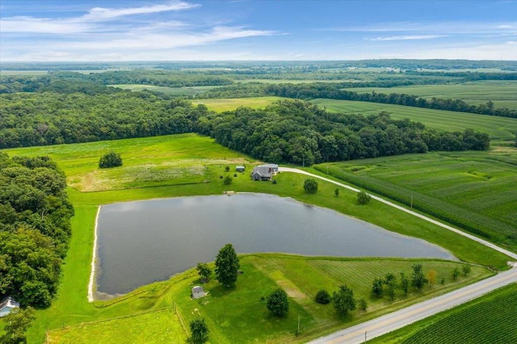 An aerial view of a large pond in the middle of a lush green field.
