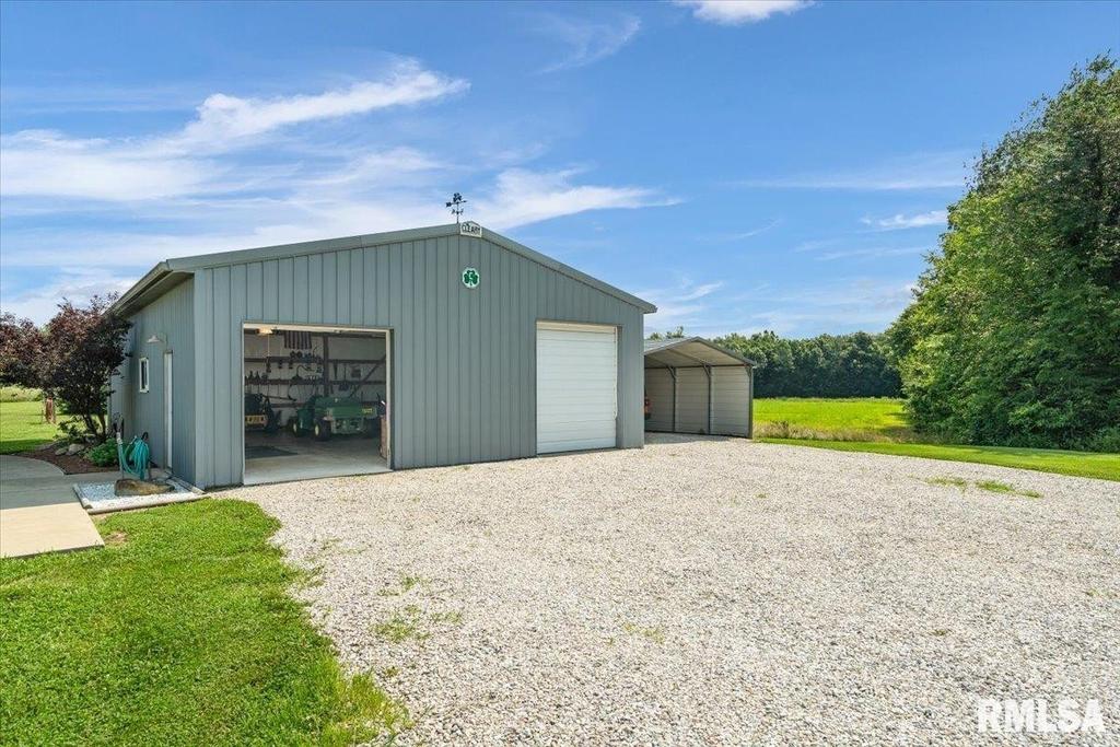 A garage with a white door is sitting in the middle of a gravel driveway.