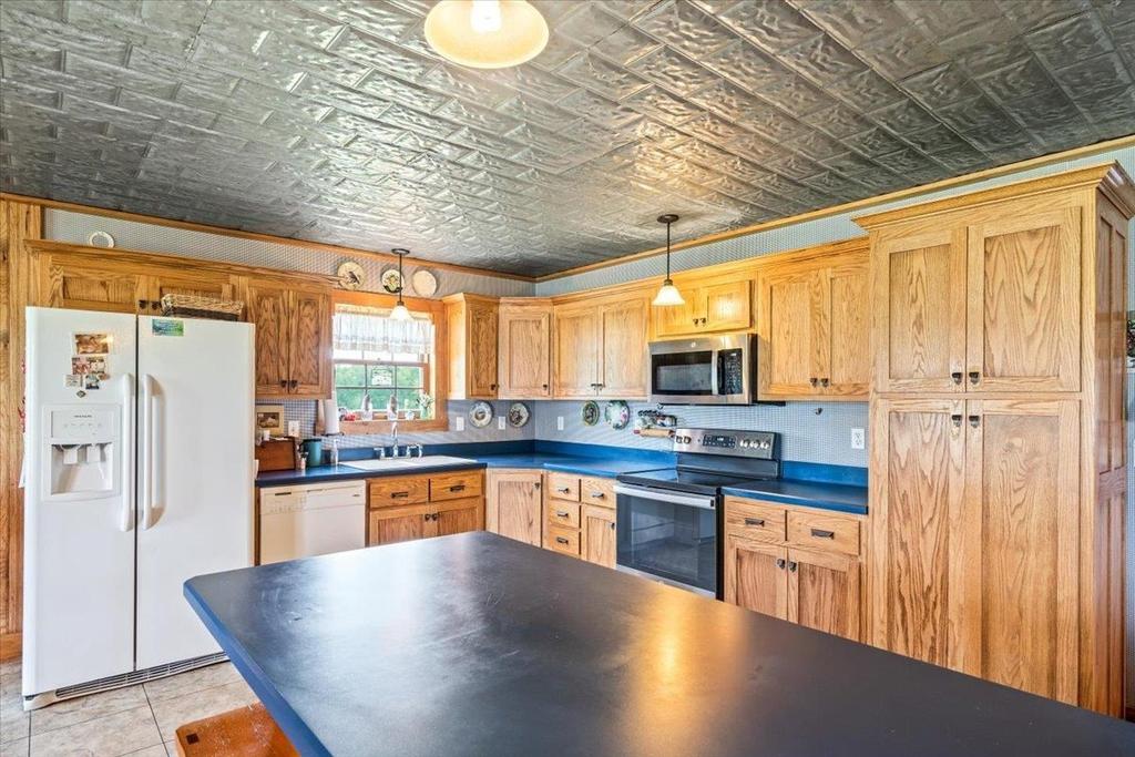 A kitchen with wooden cabinets , a refrigerator , a stove , a sink , and a large island.