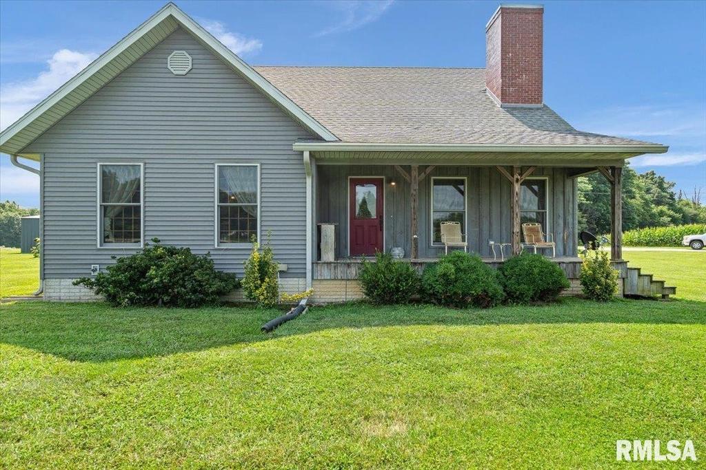 A gray house with a red door is sitting on top of a lush green field.