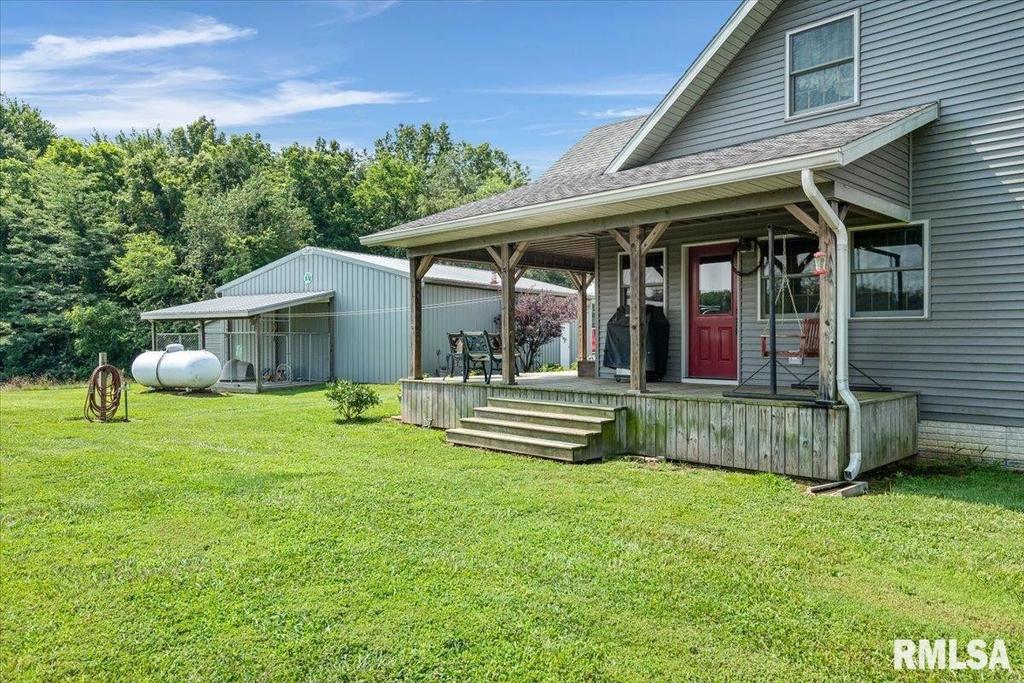 A house with a porch and a red door is sitting on top of a lush green field.