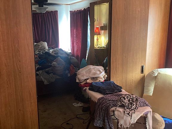 A bedroom with a lot of clothes on the floor and a mirror.