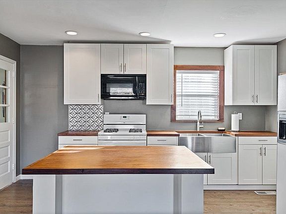 A kitchen with white cabinets , a stove , a sink , and a large island.
