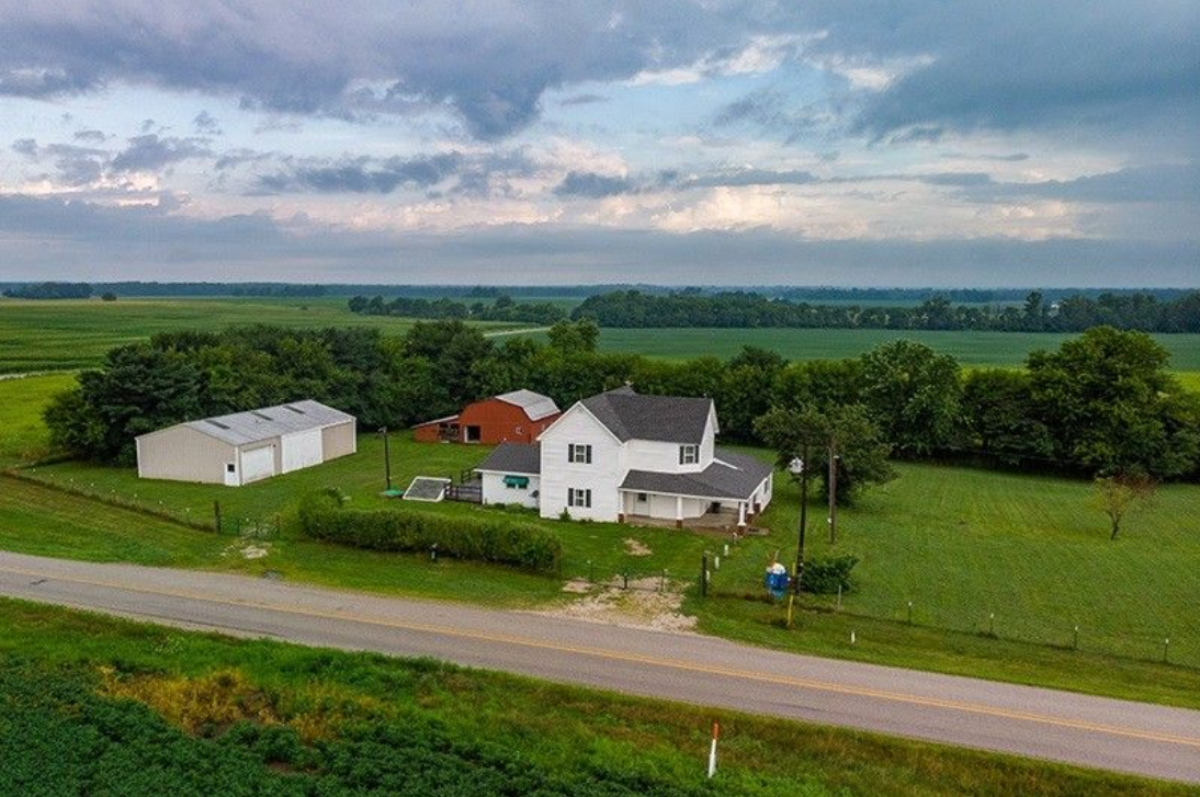 An aerial view of a house in the middle of a field next to a road.