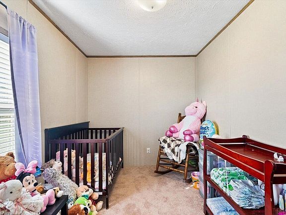 A bedroom with a crib , rocking chair , changing table and stuffed animals.
