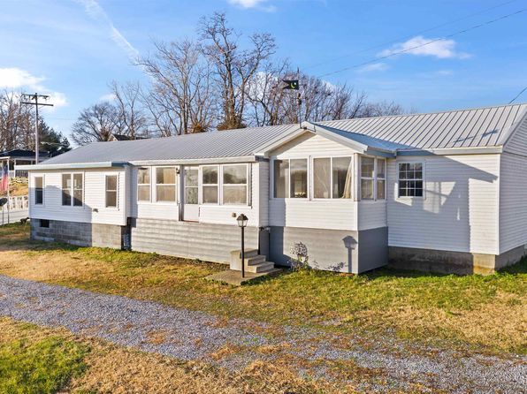 A white mobile home with a screened in porch is sitting on top of a lush green field.