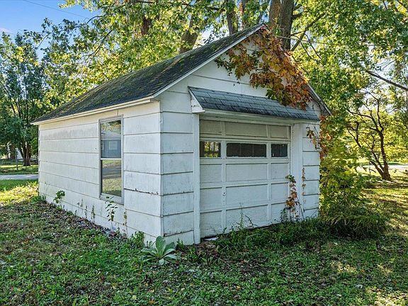 A small white garage with a black roof and a window.
