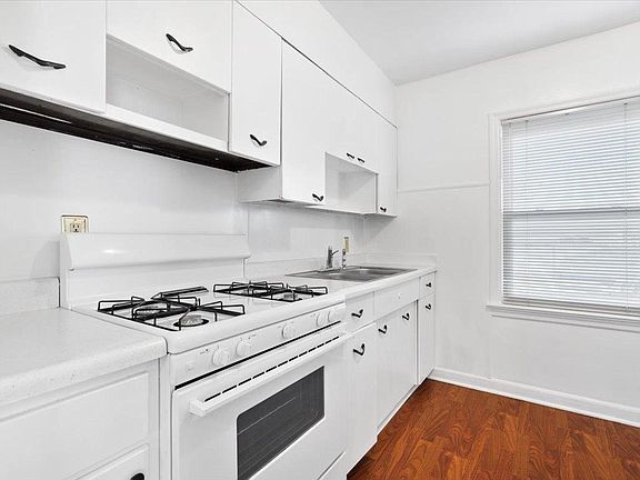 A kitchen with white cabinets , a stove , a sink , and a window.