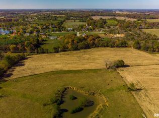 An aerial view of a lush green field with a pond in the middle.