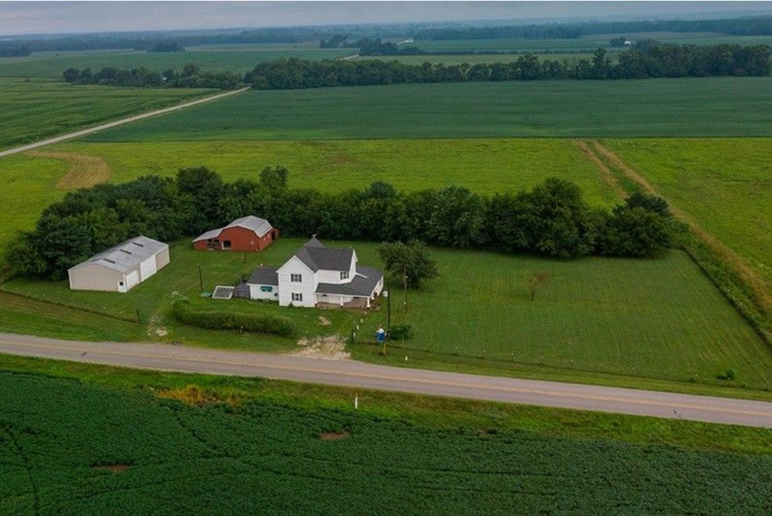 An aerial view of a farm with a house and a barn in the middle of a field.