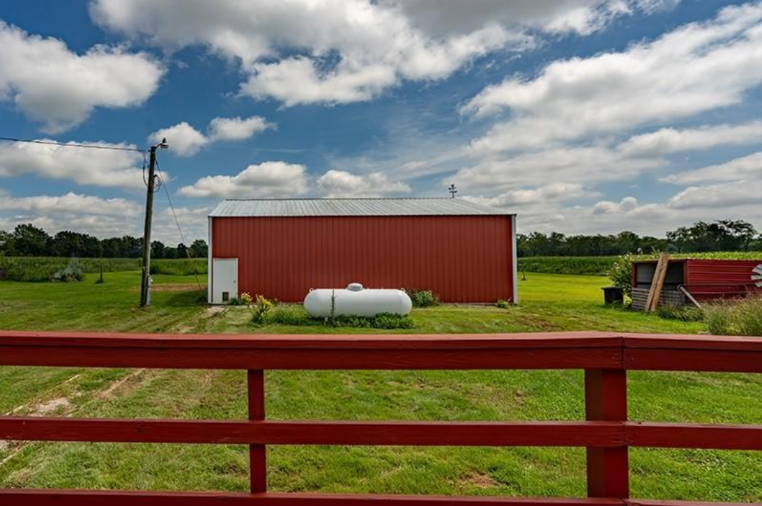A red barn is sitting in the middle of a grassy field behind a red fence.
