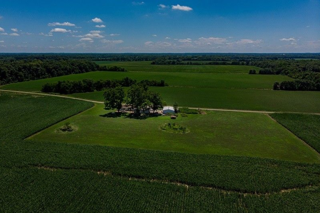 An aerial view of a large green field with a house in the middle.