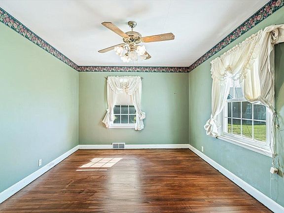 An empty room with green walls , hardwood floors , two windows and a ceiling fan.