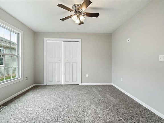 An empty room with a ceiling fan and a window.