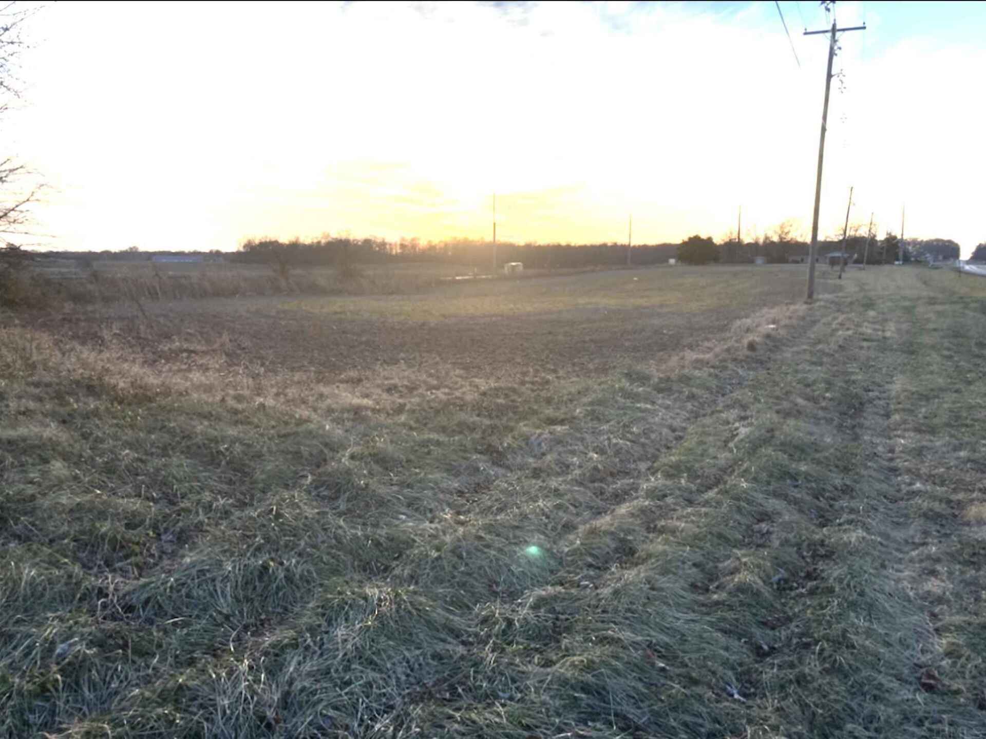 A large grassy field with a telephone pole in the foreground and a sunset in the background.
