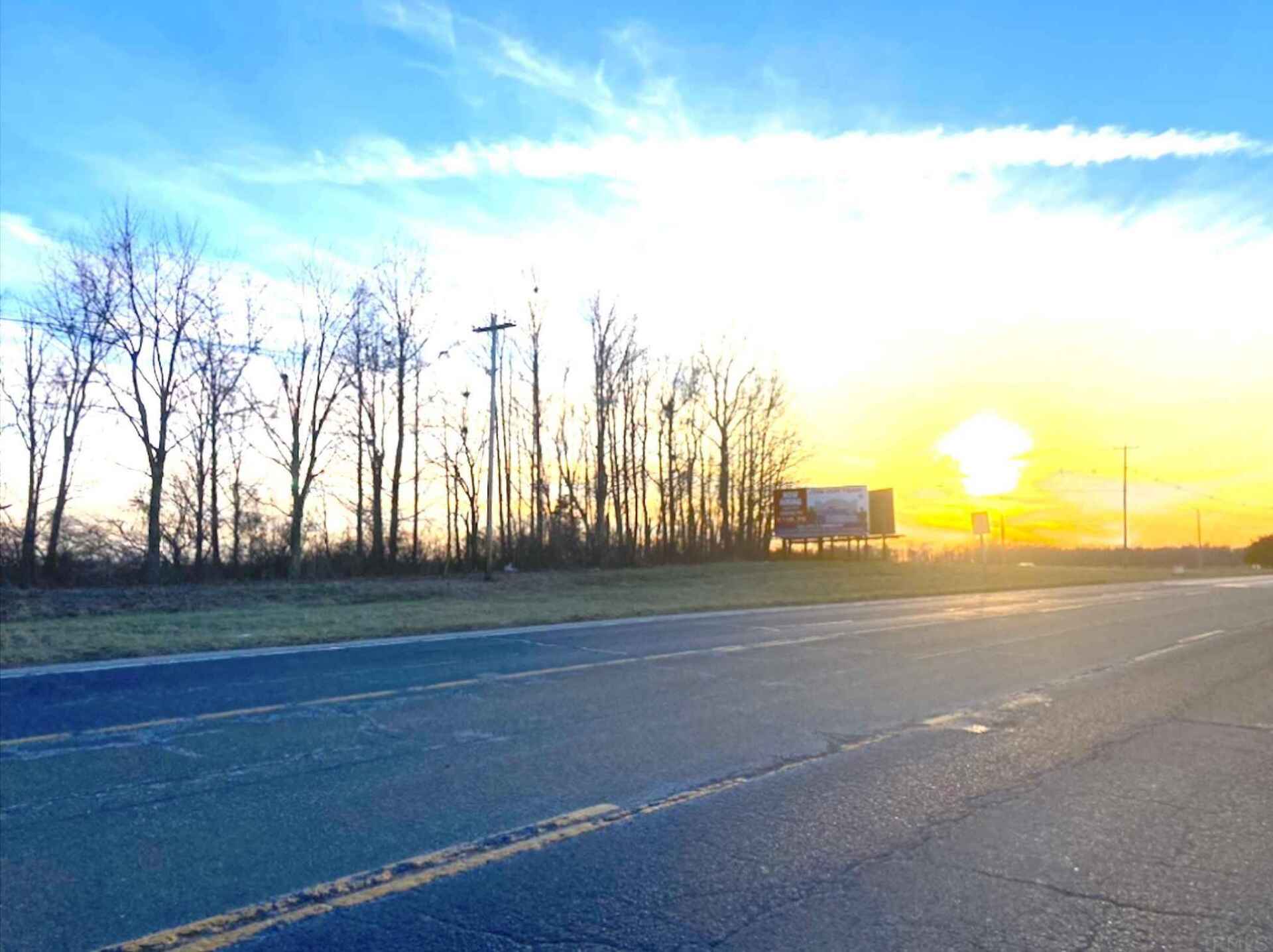 The sun is setting behind the trees on the side of the road
