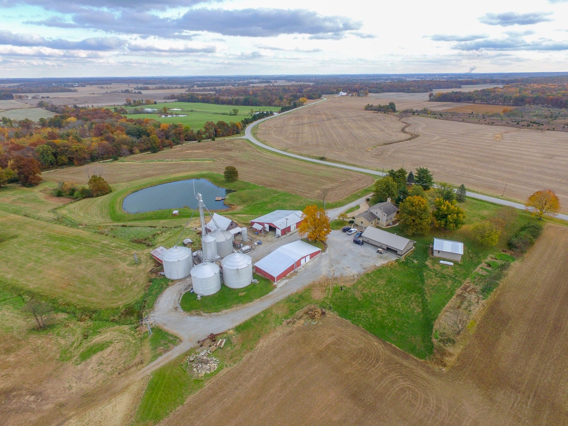 An aerial view of a farm with silos and a pond in the middle of a field.