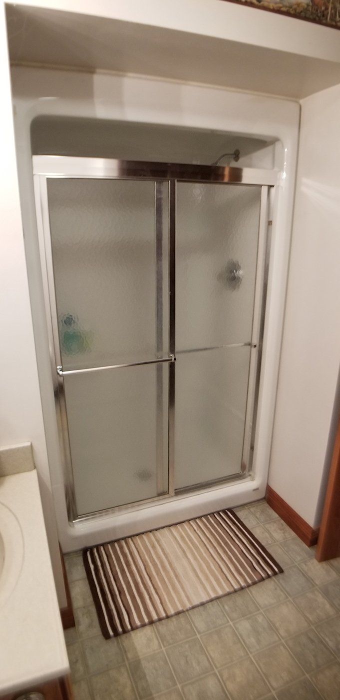 A bathroom with a sliding glass shower door and a rug on the floor.