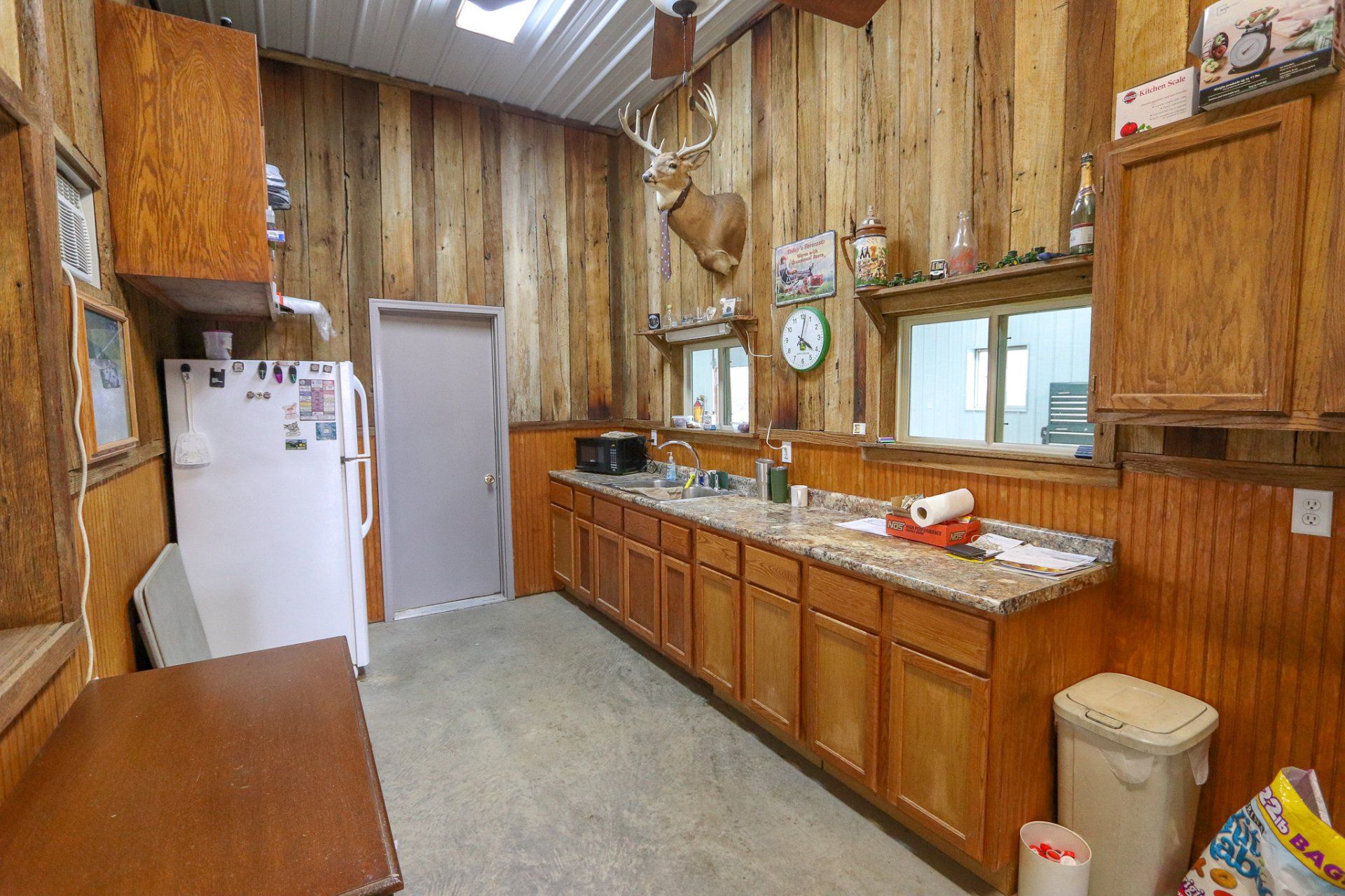 A kitchen with wooden cabinets , a refrigerator , a sink and a trash can.
