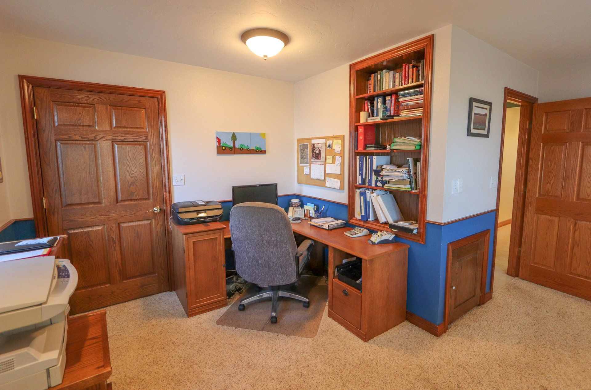 A room with a desk , chair , printer and bookshelf.