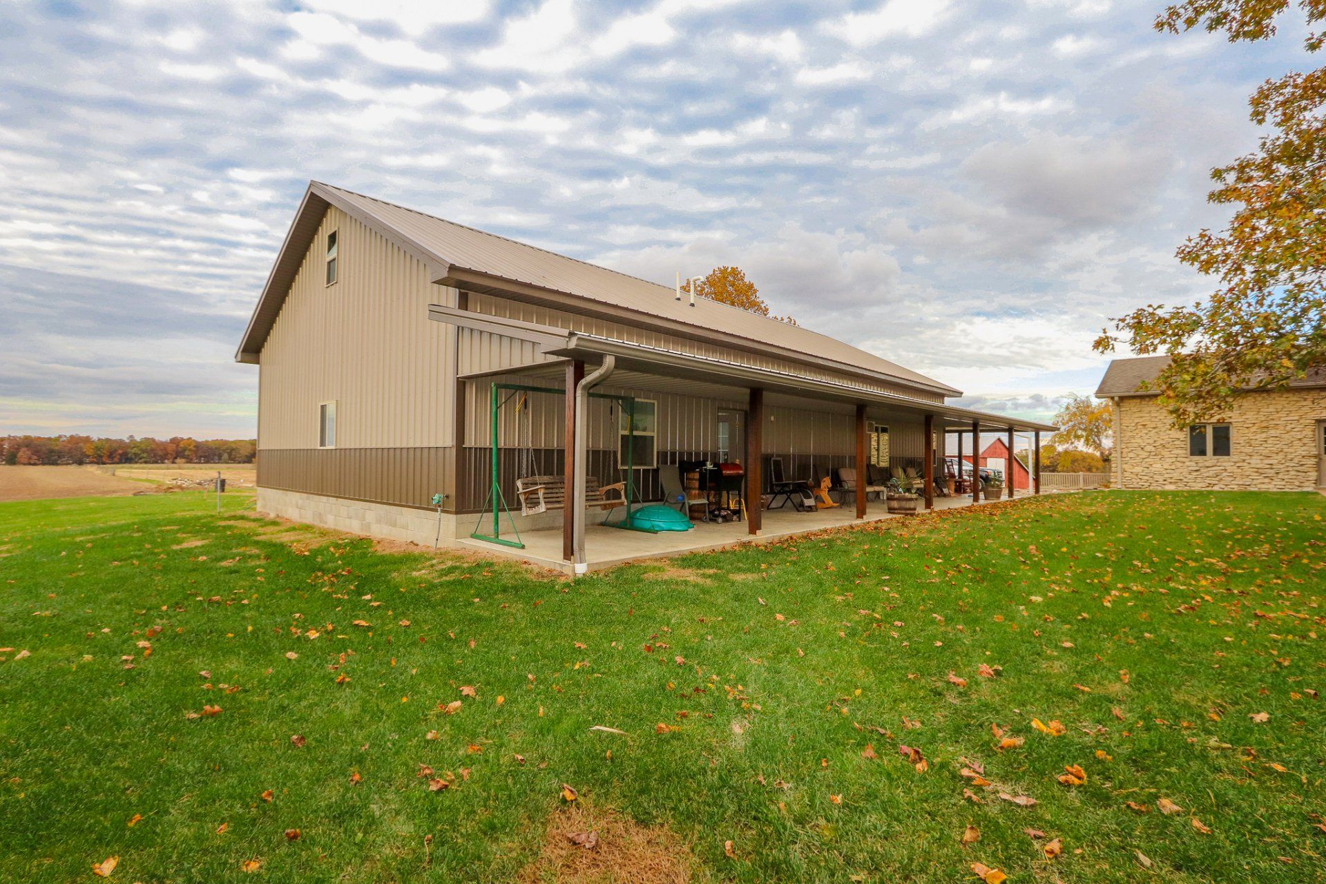 A large barn with a covered porch in the middle of a grassy field.