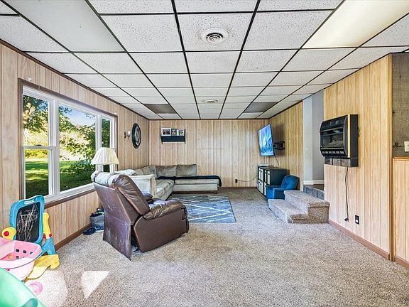 A living room with a couch , chair , television and stairs.