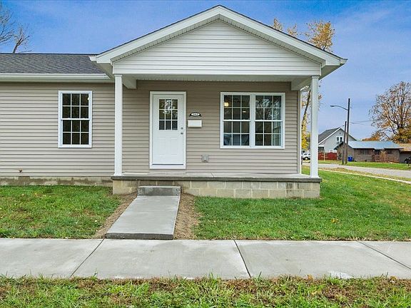 A small house with a porch and a concrete walkway leading to it.