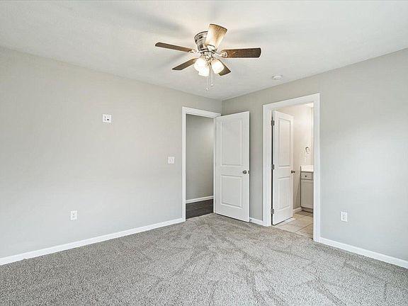 An empty bedroom with a ceiling fan and a carpeted floor.