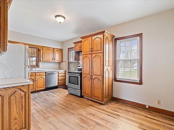 A kitchen with wooden cabinets , a stove , a refrigerator , and a window.
