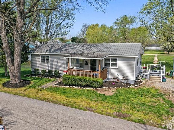 An aerial view of a small white house with a porch surrounded by trees.