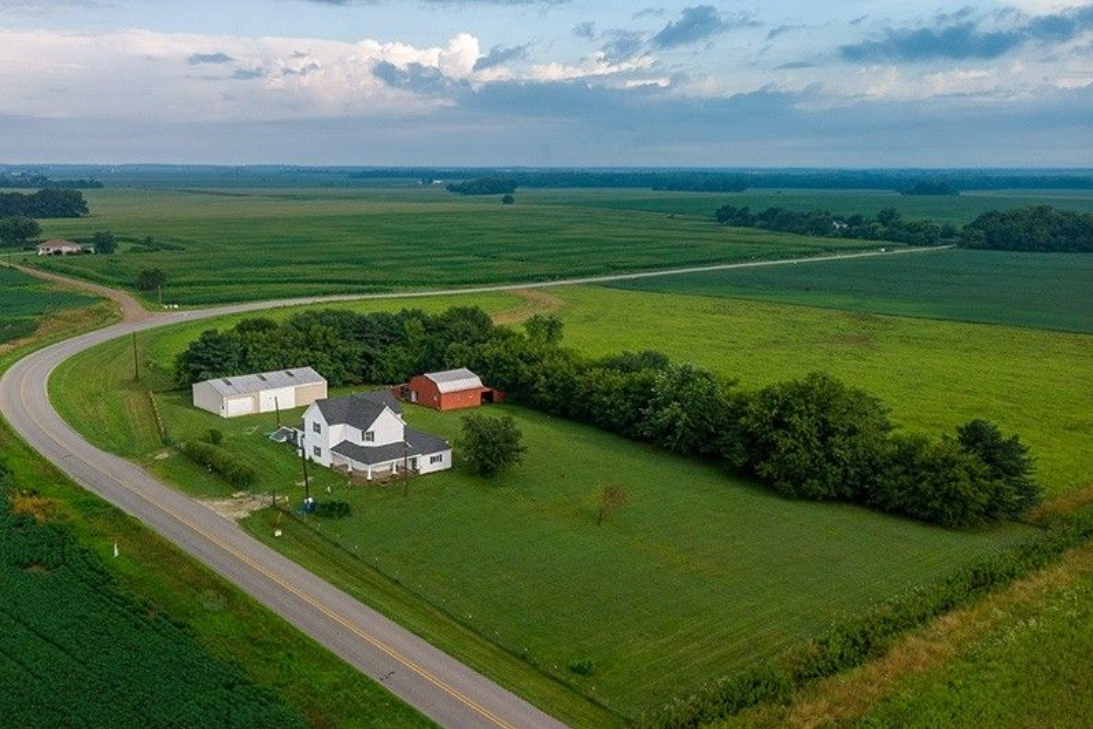 An aerial view of a farm with a house and a road going through it.