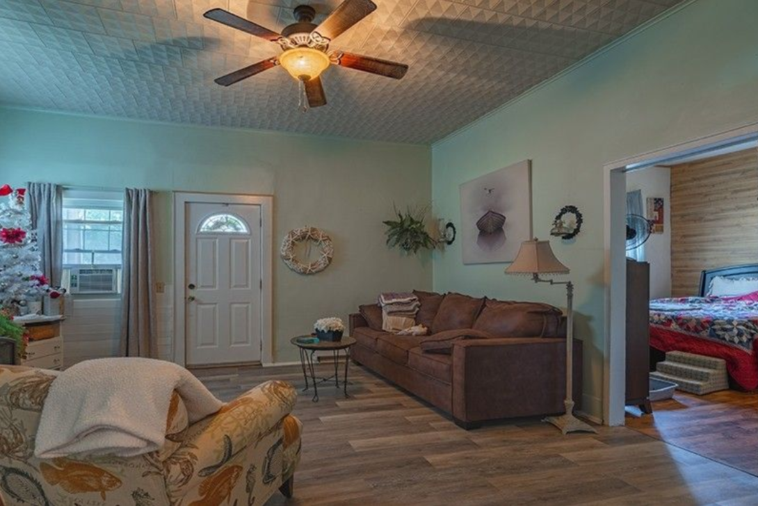 A living room with a couch , chair , table and ceiling fan.