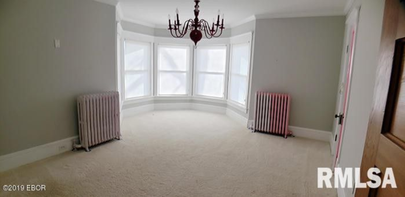 An empty room with a chandelier and two radiators.